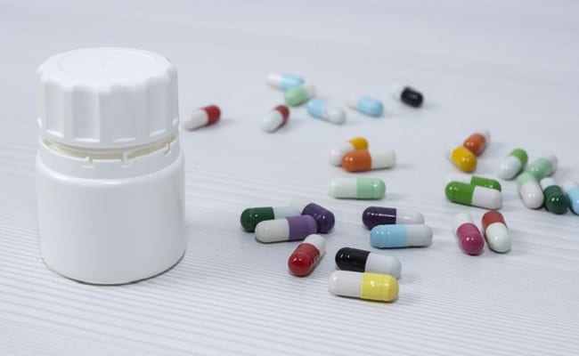 Pills scattered on a white table top next to a white pill container.
